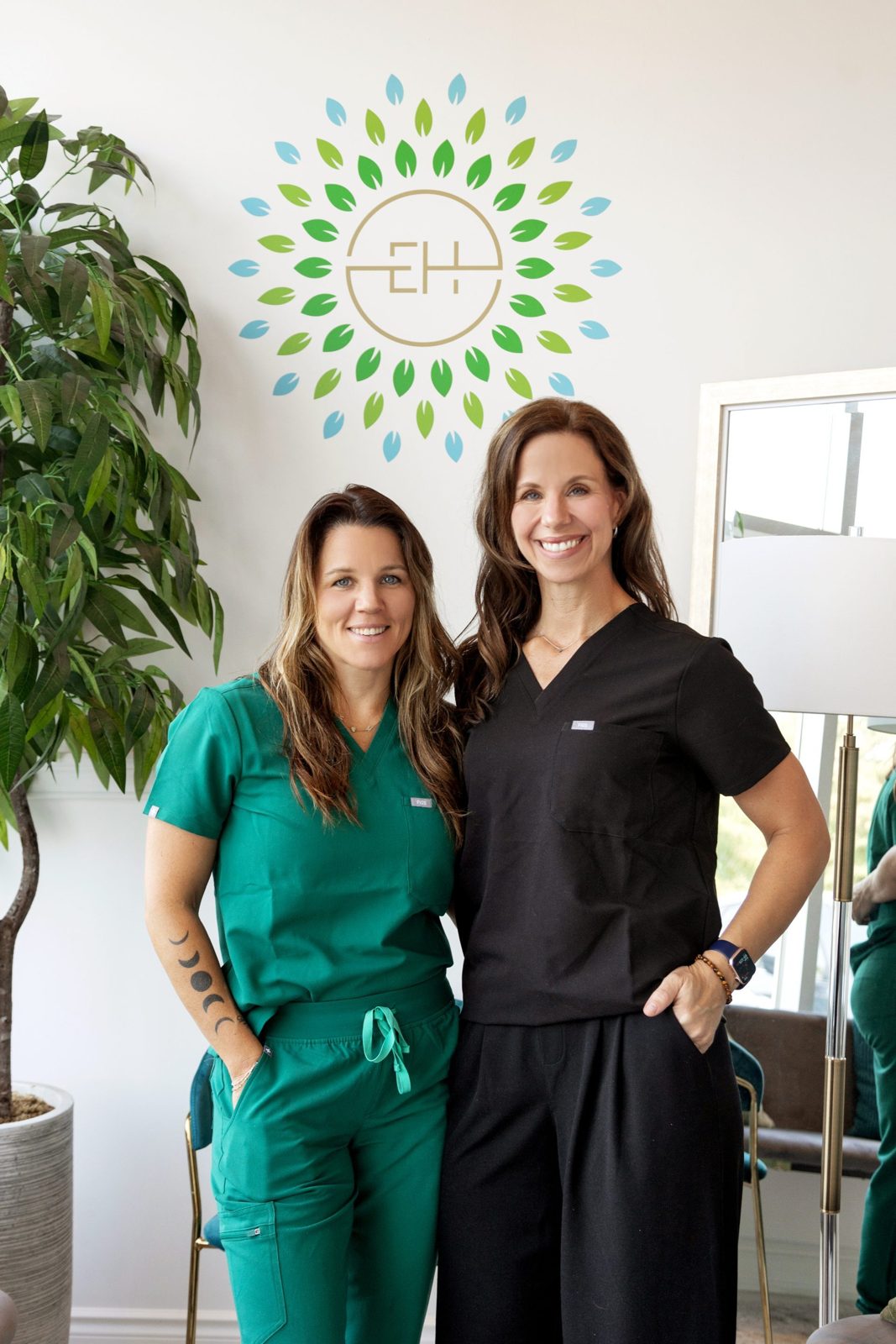 Crystal Tait and Dr. Becky Lancione, co-founders of Essential Health Clinic, standing beneath the clinic's leaf logo